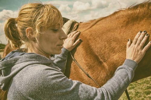 woman petting tan horse - holistic