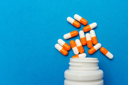orange and white capsules spilling out of bottle on bright sky blue background - adderall
