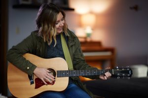 young woman playing acoustic guitar at home - creative arts