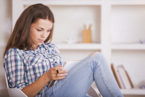 pretty young woman in a plaid shirt writing in her journal at home - journaling