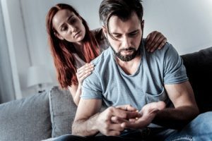 worried woman with her hands on her man's shoulders - he is holding pills in his hand - Valium addiction