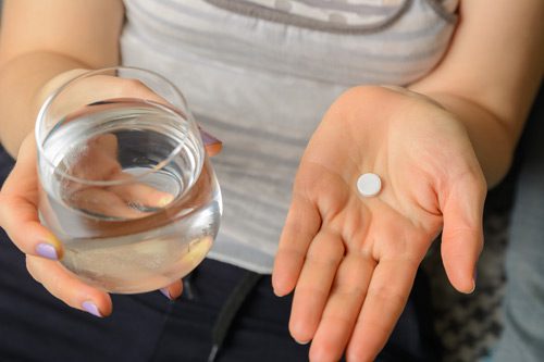 cropped shot of a woman holding a white round tablet pill and glass of water - codeine addiction