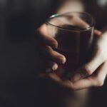 Close-up of a person's hands gently holding a glass of dark liquid
