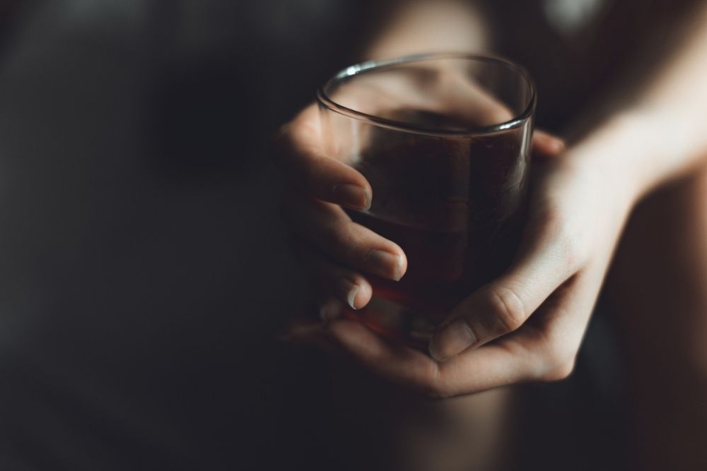 Close-up of a person's hands gently holding a glass of dark liquid