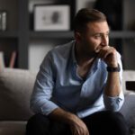 man deep in thought, sitting on couch, lonely man looking out pensively