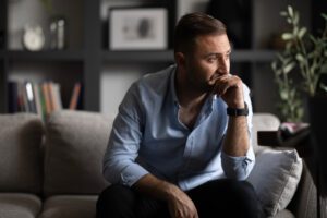 man deep in thought, sitting on couch, lonely man looking out pensively