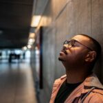 Anxiety and Substance Use(1000 x 667 px) A man wearing glasses leans against a wall with his eyes closed, appearing tense or overwhelmed, symbolizing anxiety or emotional strain.