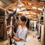 Woman gently holding and interacting with a horse inside a stable, suggesting a calm therapeutic or bonding moment.