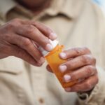 Prescription Medication 1000 x 667 A person holds an orange prescription pill bottle, removing the cap while preparing to take medication.