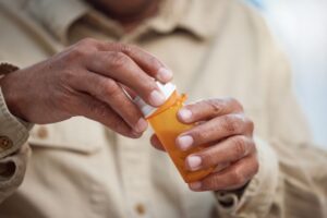 A person holds an orange prescription pill bottle, removing the cap while preparing to take medication.