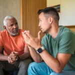 English Mountain – How Does a Co-Occurring Disorder Program Work – Edited Two men discussing something while seated on a couch, surrounded by a warm and inviting living room atmosphere.