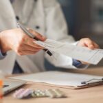 English Mountain – What You Should Know About Prescription and Opioid Misuse – Edited English Mountain - What You Should Know About Prescription and Opioid Misuse. A doctor in a lab coat hands a prescription sheet to an unidentified individual as prescription drugs sit on a table.