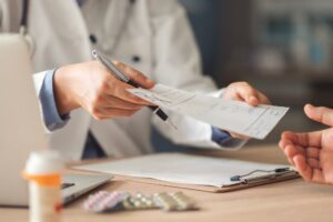 English Mountain - What You Should Know About Prescription and Opioid Misuse. A doctor in a lab coat hands a prescription sheet to an unidentified individual as prescription drugs sit on a table.