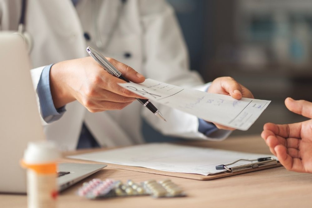 English Mountain - What You Should Know About Prescription and Opioid Misuse. A doctor in a lab coat hands a prescription sheet to an unidentified individual as prescription drugs sit on a table.
